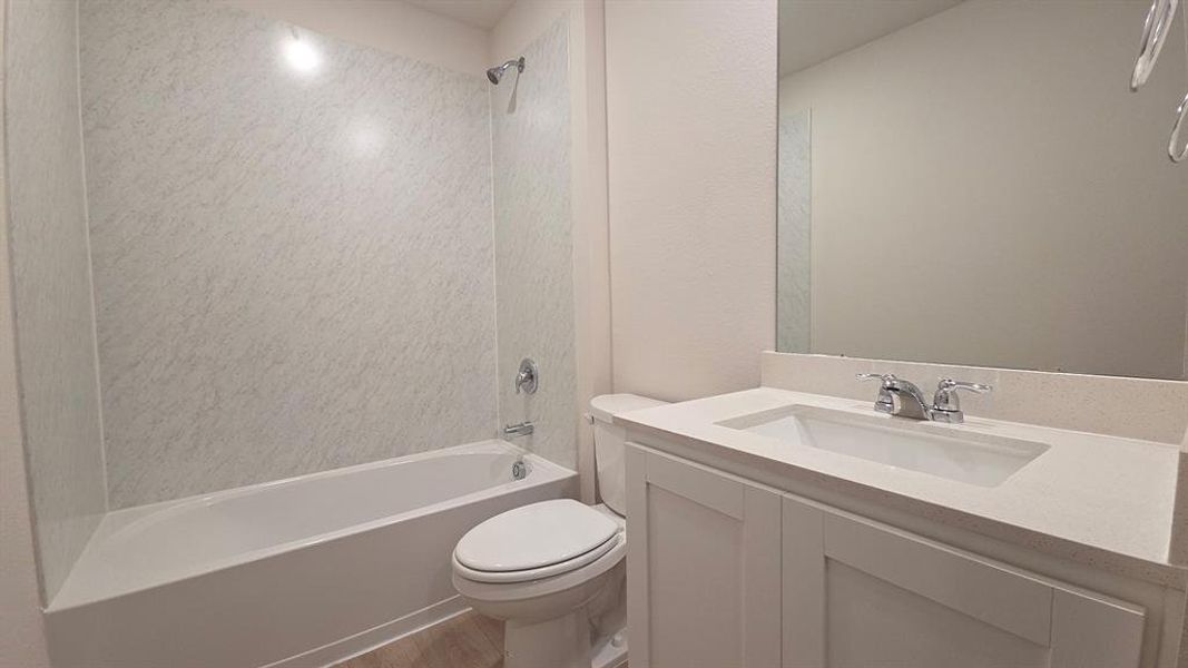 Bathroom featuring a white bathtub and shower surround, a white vanity with an integrated sink, a light-toned countertop, and chrome fixtures Bathroom featuring a white bathtub and shower surround, a white vanity with an integrated sink, a light-toned countertop, and chrome fixtures