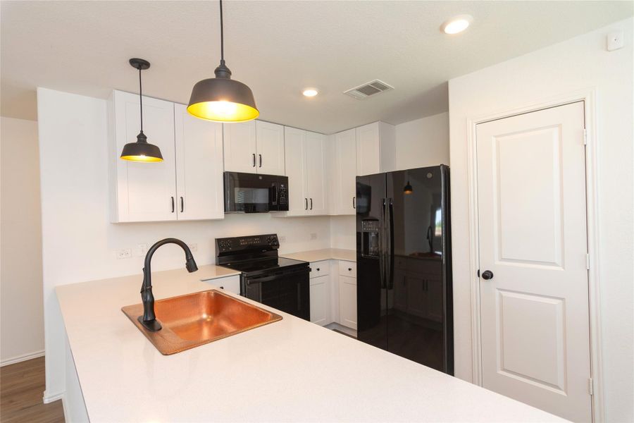 Kitchen with white cabinetry, black appliances, a copper sink with a oil-rubbed bronze faucet, and pendant lighting