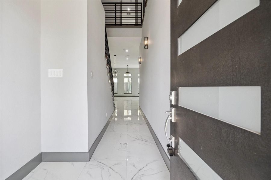 Modern entry sets the tone with porcelain tile floors, crisp lines, and generous natural light. The double-height ceiling and open railing above lead the eye toward the main living areas, establishing a refined sense of arrival.