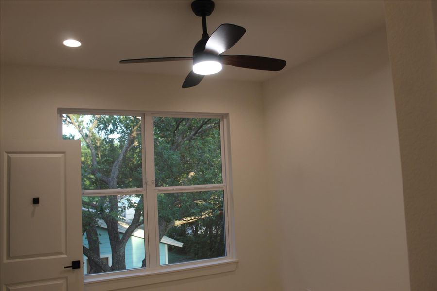 A window frames a verdant outdoor scene, complemented by a modern ceiling fan and recessed lighting.