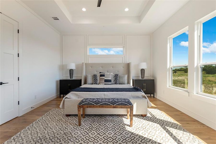 Bedroom with light hardwood / wood-style floors, a tray ceiling, and ceiling fan