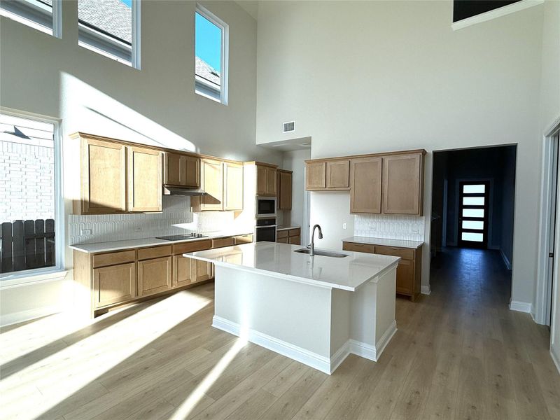 Kitchen featuring tasteful backsplash, light stone countertops, appliances with stainless steel finishes, a center island with sink, and light wood-type flooring