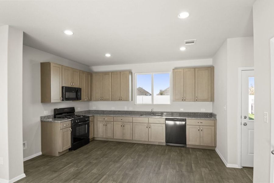 Image of a kitchen with light brown cabinets, granite countertops, black appliances and dark vinyl flooring