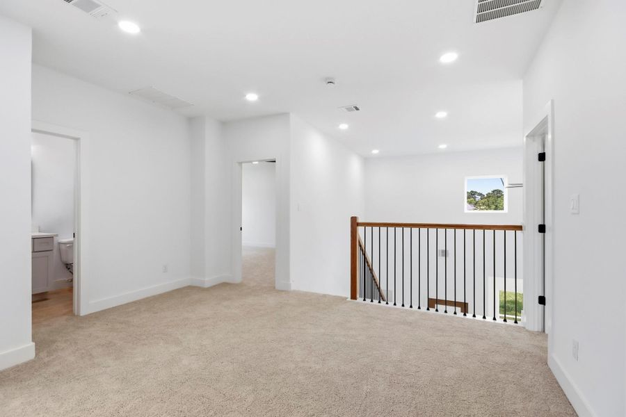 Bright and spacious upstairs landing with plush carpeting, recessed lighting, and elegant wood-and-iron railing, offering access to multiple rooms and a bathroom.