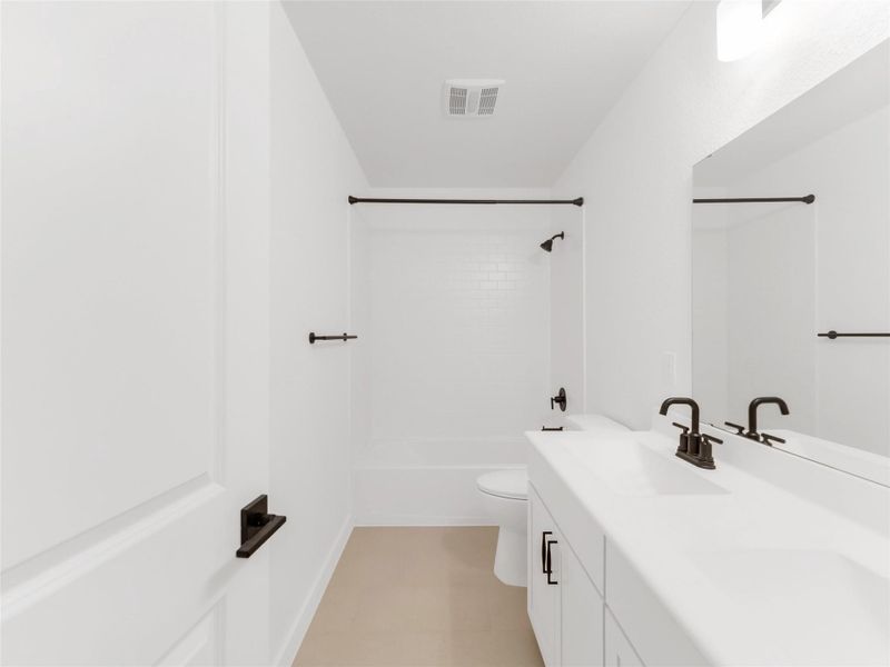 Secondary bathroom with a clean white aesthetic. It features a spacious vanity with dual sinks, sleek black fixtures, and a combination bathtub and shower.
