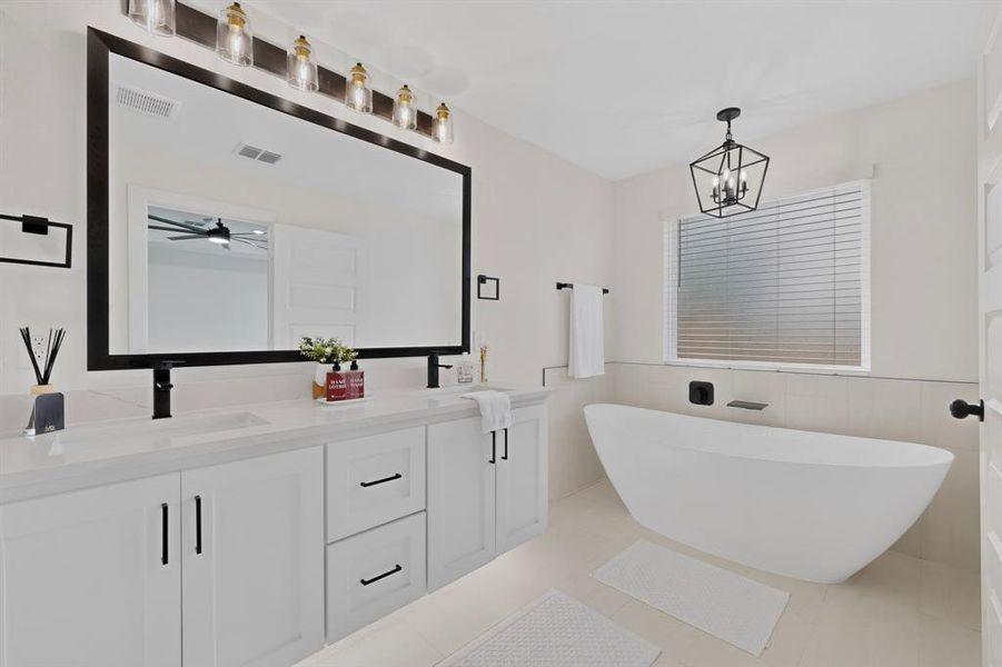 Contemporary bathroom featuring a freestanding soaking tub, a dual vanity with white cabinetry, quartz countertops, and matte black fixtures