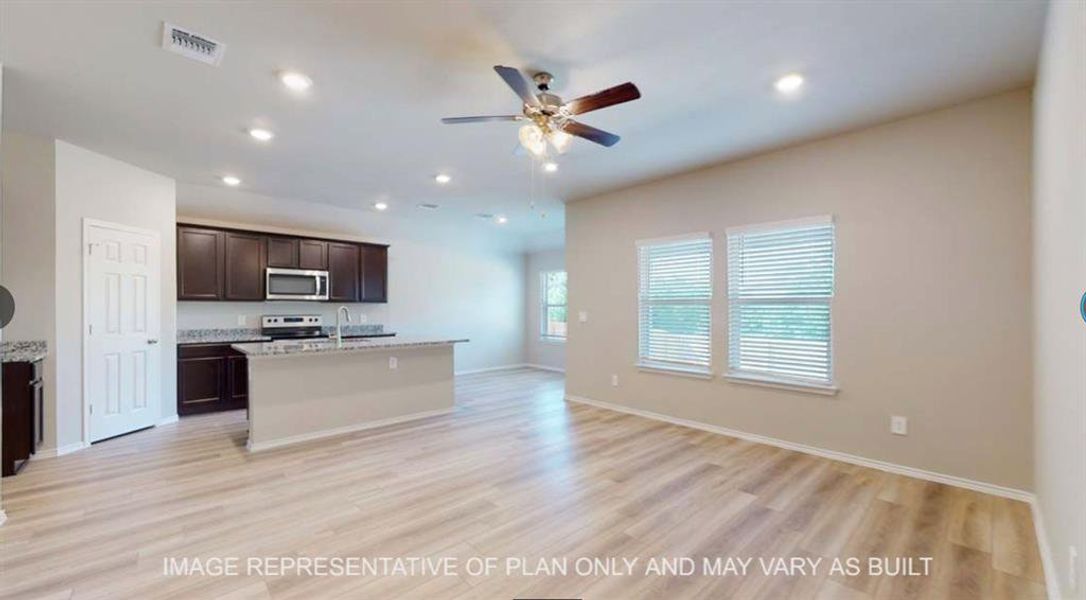 Kitchen with dark wood finish cabinets, open floor plan, a ceiling fan, a center island with sink, and light wood-style floors