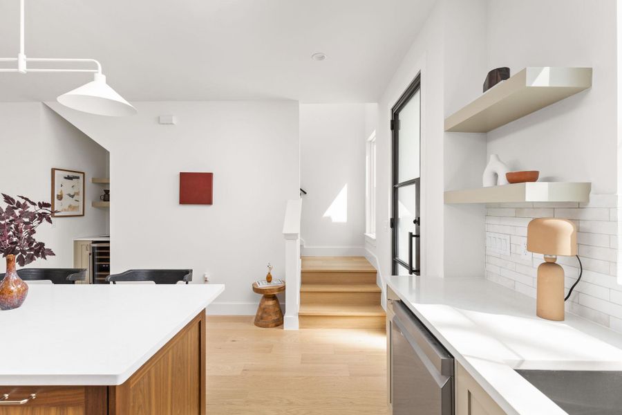 Kitchen with open shelves, light wood-type flooring, stainless steel dishwasher, wine cooler, and decorative light fixtures