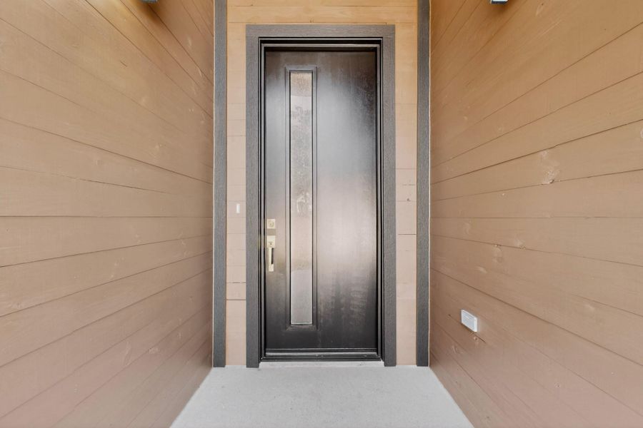 A dark, modern door with a sleek glass insert welcomes visitors, framed by warm horizontal siding.