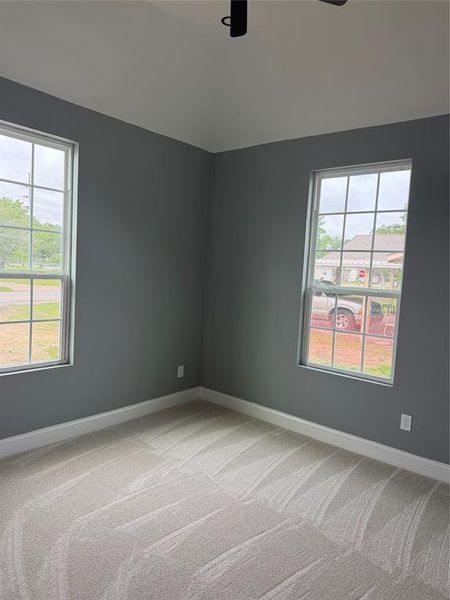 Room featuring two windows with grid patterns, light-toned carpeting, and a vaulted ceiling