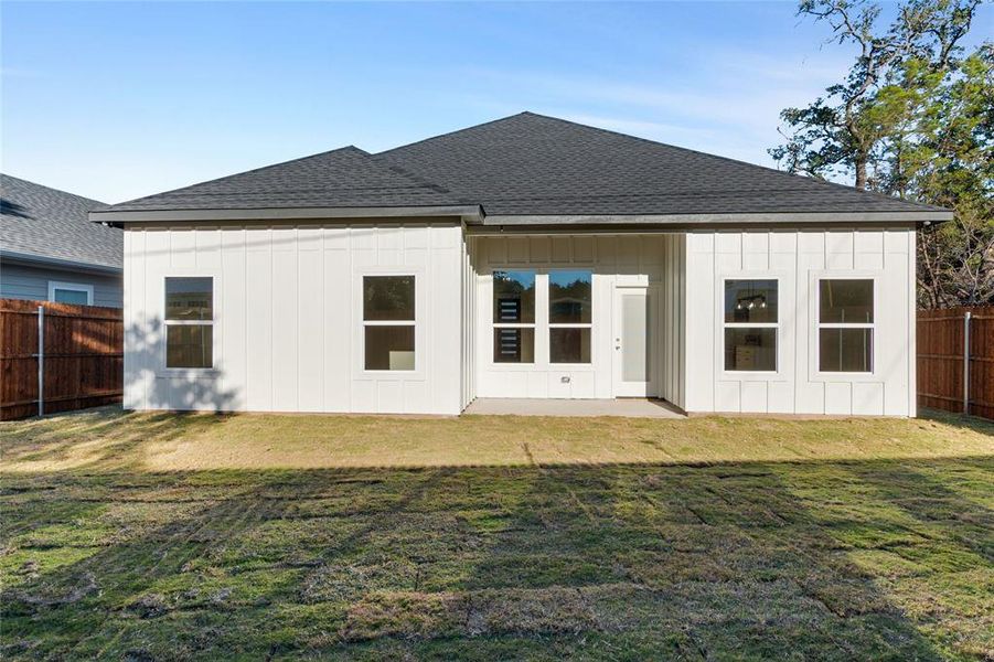 Rear view of property with roof with shingles, a fenced backyard, and a patio area