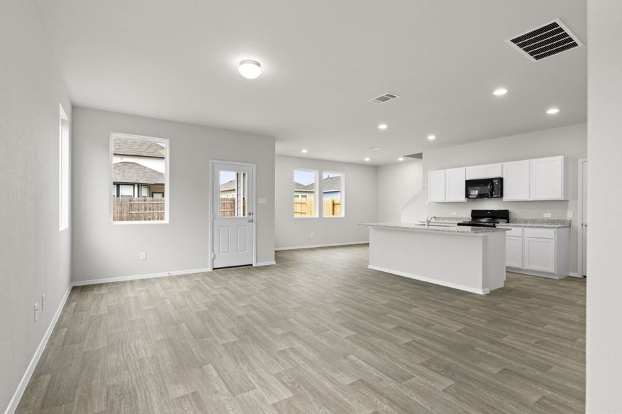 Image of a living room area with an open kitchen with cream walls, a white back door and windows