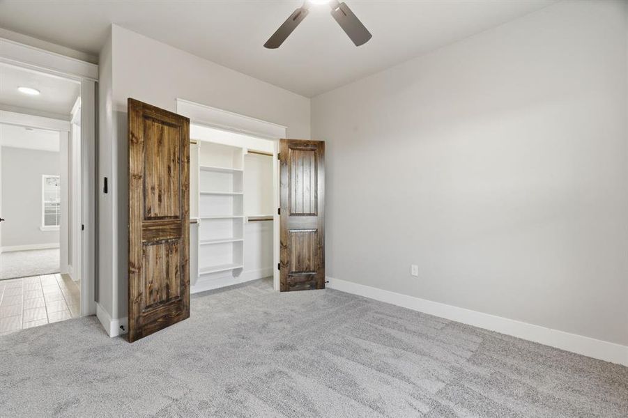 Unfurnished bedroom featuring light colored carpet, a spacious closet, and a ceiling fan