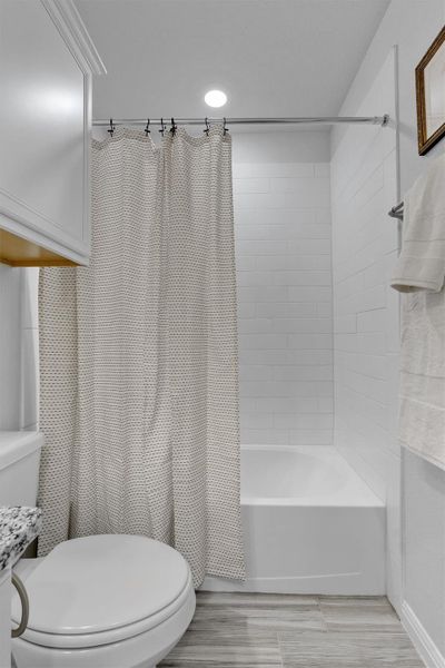 Bathroom featuring toilet and shower / bathtub combination with curtain