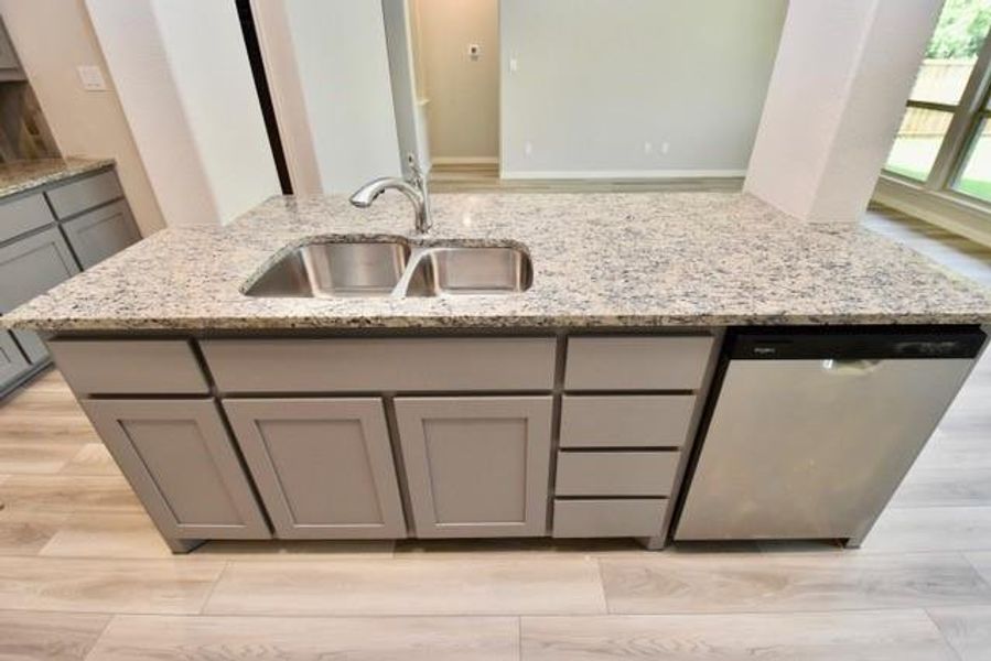 Kitchen with gray cabinets, dishwasher, light stone counters, and light wood-style floors