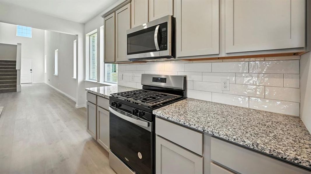 Kitchen with appliances with stainless steel finishes, light stone countertops, healthy amount of natural light, and light wood-type flooring Kitchen with appliances with stainless steel finishes, light stone countertops, healthy amount of natural light, and light wood-type flooring