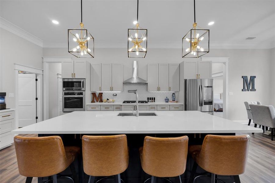 Kitchen with wall chimney exhaust hood, tasteful backsplash, a spacious island, white cabinets, and appliances with stainless steel finishes