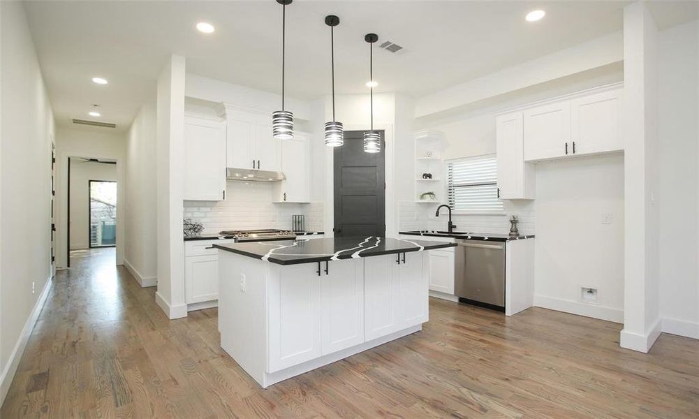 This modern kitchen features sleek white cabinetry, a stylish black quartz countertop with bar seating for 3.