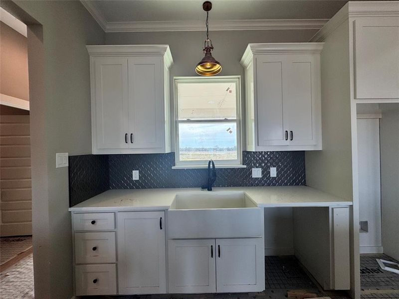 Kitchen with tasteful backsplash, white cabinetry, crown molding, and sink