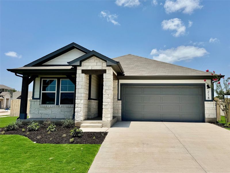 View of front of house featuring stone siding, driveway, an attached garage, a front yard, and a shingled roof