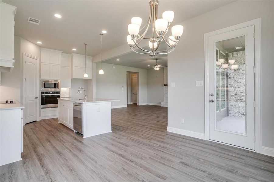 Kitchen with white cabinetry, an island with sink, stainless steel appliances, light hardwood / wood-style floors, and pendant lighting