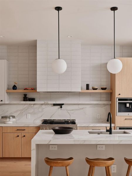 Contemporary kitchen featuring light wood-finish cabinetry, white slab backsplash, marble-look countertops, and recessed lighting