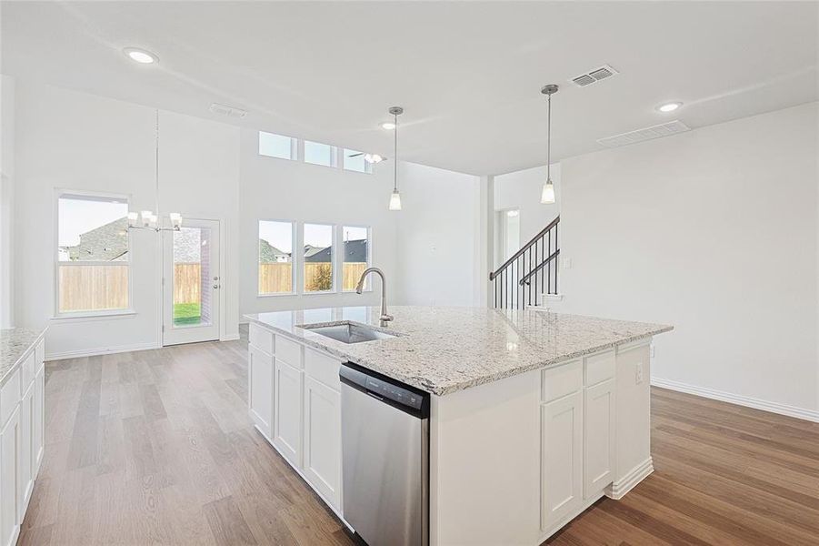 Kitchen with white cabinetry, dishwasher, sink, light hardwood / wood-style flooring, and a center island with sink