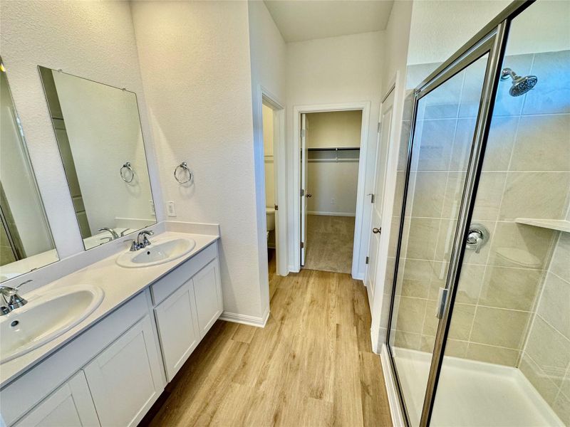 Bathroom featuring a spacious closet, double vanity, light wood-type flooring, a stall shower, and a textured wall