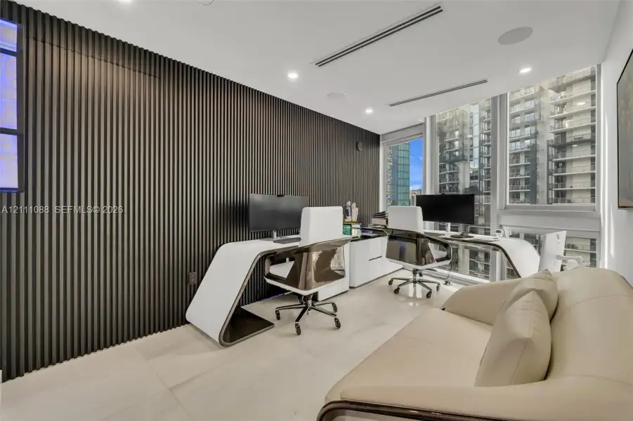 Interior space featuring a full-height, dark-toned slat wall treatment, neutral-toned large-format flooring, recessed ceiling lighting, integrated audio speakers, and expansive floor-to-ceiling windows Interior space featuring a full-height, dark-toned slat wall treatment, neutral-toned large-format flooring, recessed ceiling lighting, integrated audio speakers, and expansive floor-to-ceiling windows