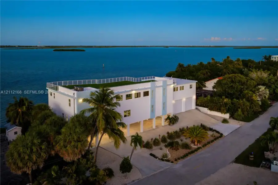 Multi-story waterfront residence featuring a rooftop terrace, elevated construction, multi-car garage, and established landscaping Multi-story waterfront residence featuring a rooftop terrace, elevated construction, multi-car garage, and established landscaping