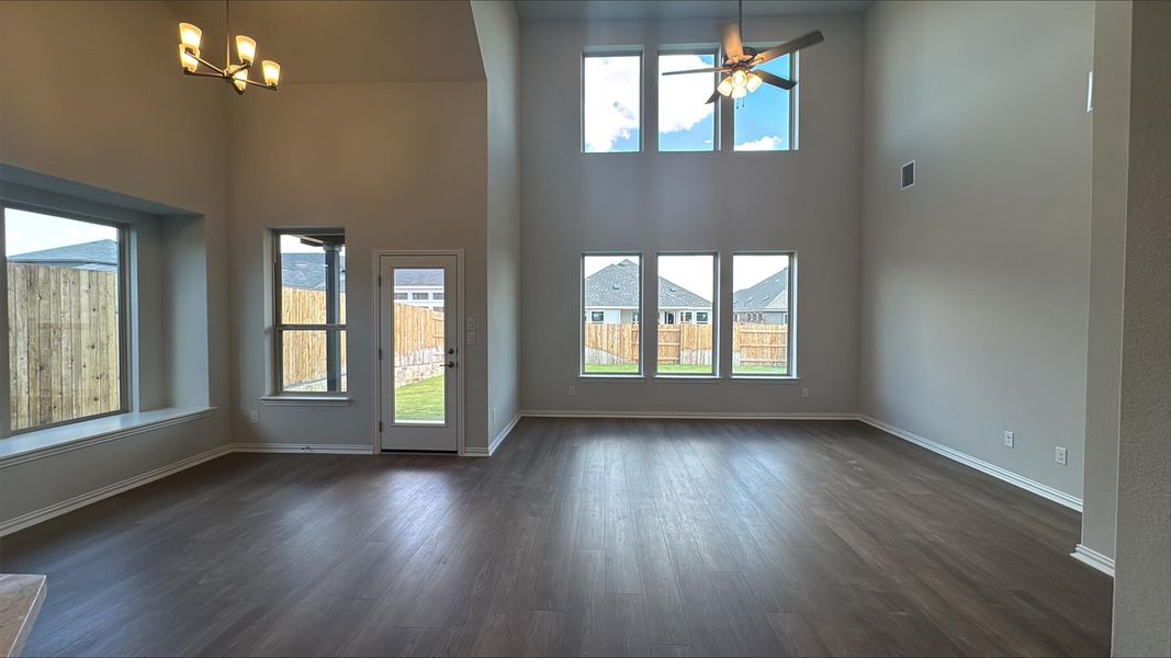 Unfurnished living room featuring a high ceiling, dark wood-style flooring, a ceiling fan, and a chandelier Unfurnished living room featuring a high ceiling, dark wood-style flooring, a ceiling fan, and a chandelier
