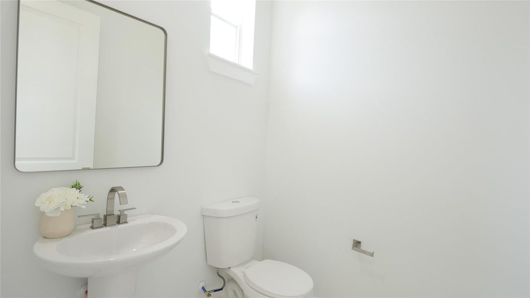 This photo shows a bright, minimalist bathroom featuring a white pedestal sink, a modern mirror, and a toilet. There is a small window for natural light, and the walls are painted white for a clean look. This photo shows a bright, minimalist bathroom featuring a white pedestal sink, a modern mirror, and a toilet. There is a small window for natural light, and the walls are painted white for a clean look.