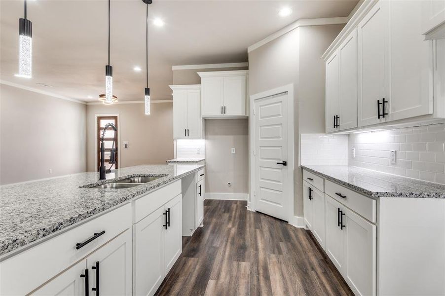 Kitchen featuring dark wood-style flooring, tasteful backsplash, white cabinets, light stone countertops, and crown molding