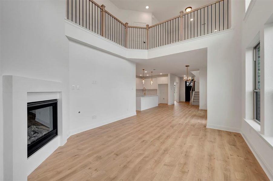 Unfurnished living room featuring hanging lights, a glass covered fireplace, light wood-type flooring, and a high ceiling