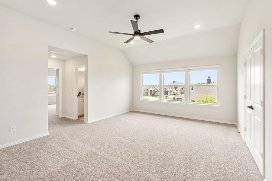 Empty bedroom with vaulted ceiling, ceiling fan, carpet flooring, and large triple window Empty bedroom with vaulted ceiling, ceiling fan, carpet flooring, and large triple window