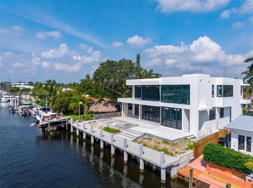Contemporary waterfront residence featuring a concrete dock, expansive glass-paneled exterior, dual-level outdoor terrace, and a built-in fire feature Contemporary waterfront residence featuring a concrete dock, expansive glass-paneled exterior, dual-level outdoor terrace, and a built-in fire feature