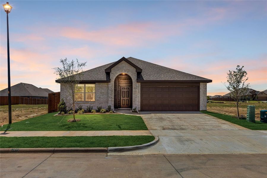 Single-story brick home with arched entry door, two-car garage, and concrete driveway