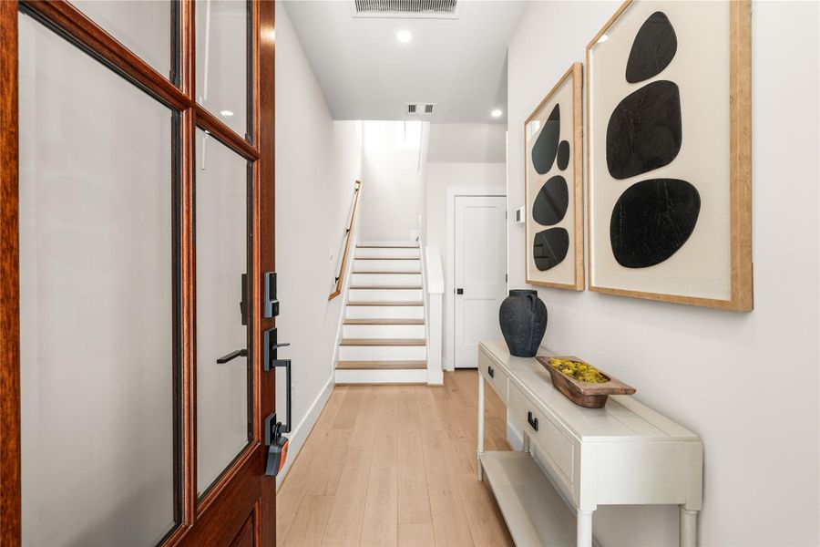 The entry establishes a clean transition into the home, with warm-toned flooring, a glass-paneled front door, and stairs leading to the main living level.