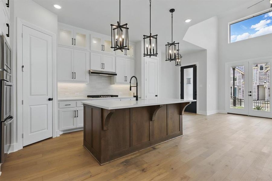 Kitchen featuring glass insert cabinets, white cabinets, a kitchen breakfast bar, tasteful backsplash, and a center island with sink