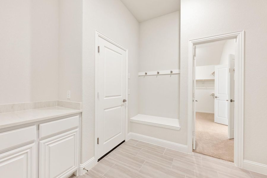 Mudroom with built-in bench, coat hooks, white cabinets, and doorway leading to carpeted walk-in closet