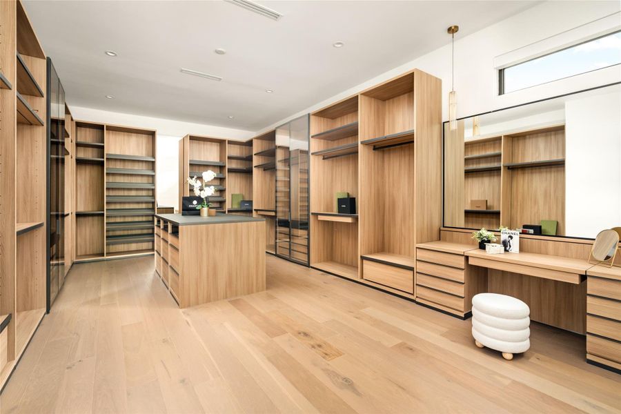 Expansive primary walk-in closet featuring floor-to-ceiling built-ins, a central island, and a dedicated vanity area.