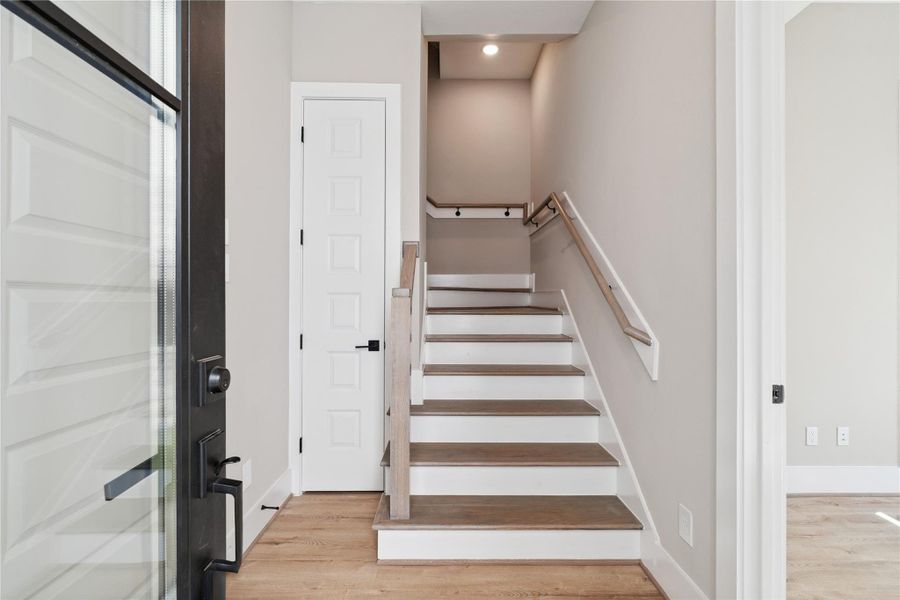 A minimalist entry hall welcomes with wide-plank flooring and a softly winding staircase, setting a quiet architectural tone from the outset.