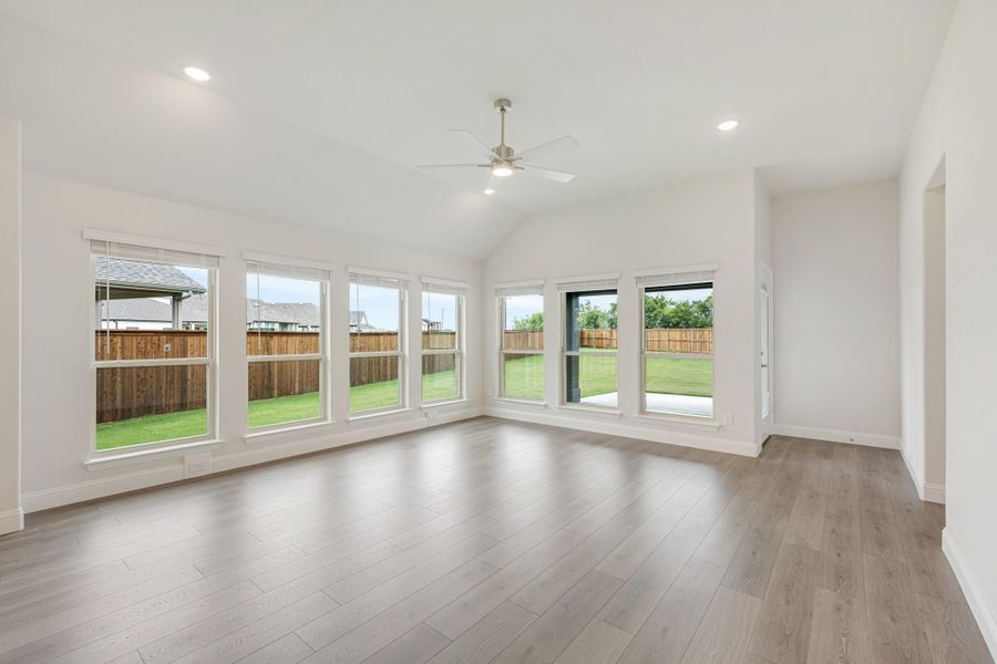 Empty living room with vaulted ceiling, ceiling fan, hardwood floors, and large windows overlooking backyard Empty living room with vaulted ceiling, ceiling fan, hardwood floors, and large windows overlooking backyard
