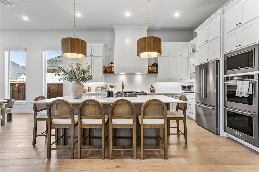 Gorgeous kitchen with designer lighting, oversized island, extensive cabinetry, & a custom hood vent with open shelving.