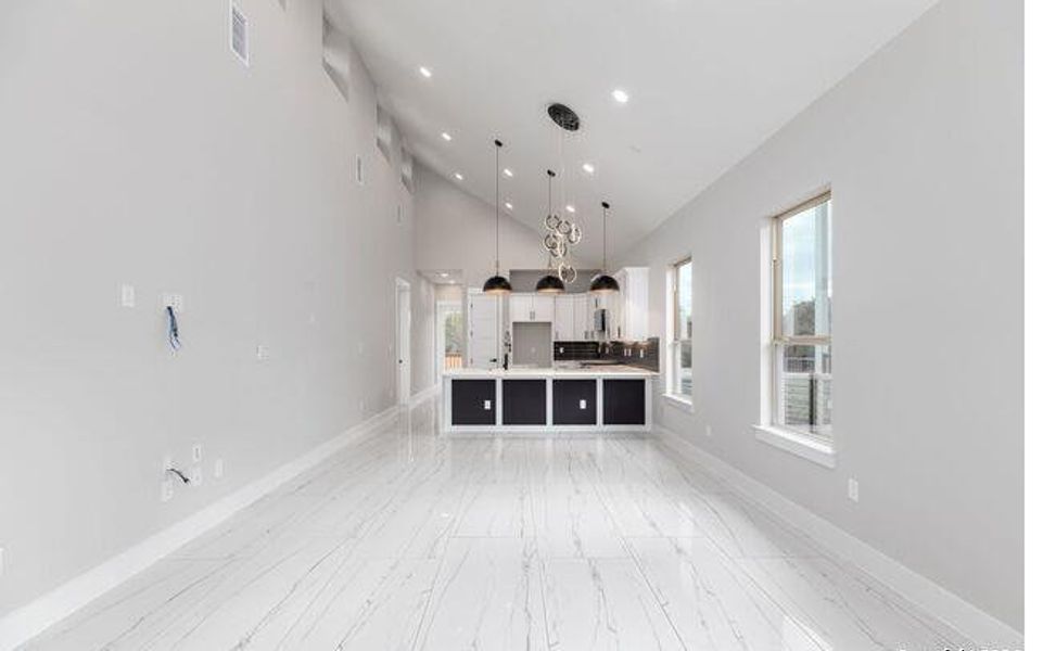 Open-concept living area featuring a vaulted ceiling with recessed lighting, large windows, and white marble-look tile flooring