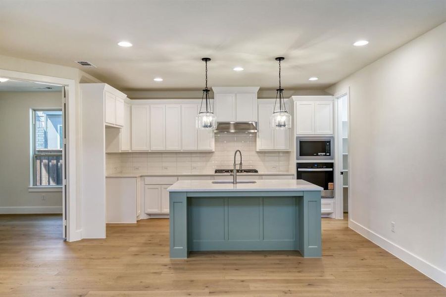Two tone kitchen featuring an island with sink, decorative light fixtures, two tone cabinets, stainless steel appliances, and light wood-type flooring Two tone kitchen featuring an island with sink, decorative light fixtures, two tone cabinets, stainless steel appliances, and light wood-type flooring