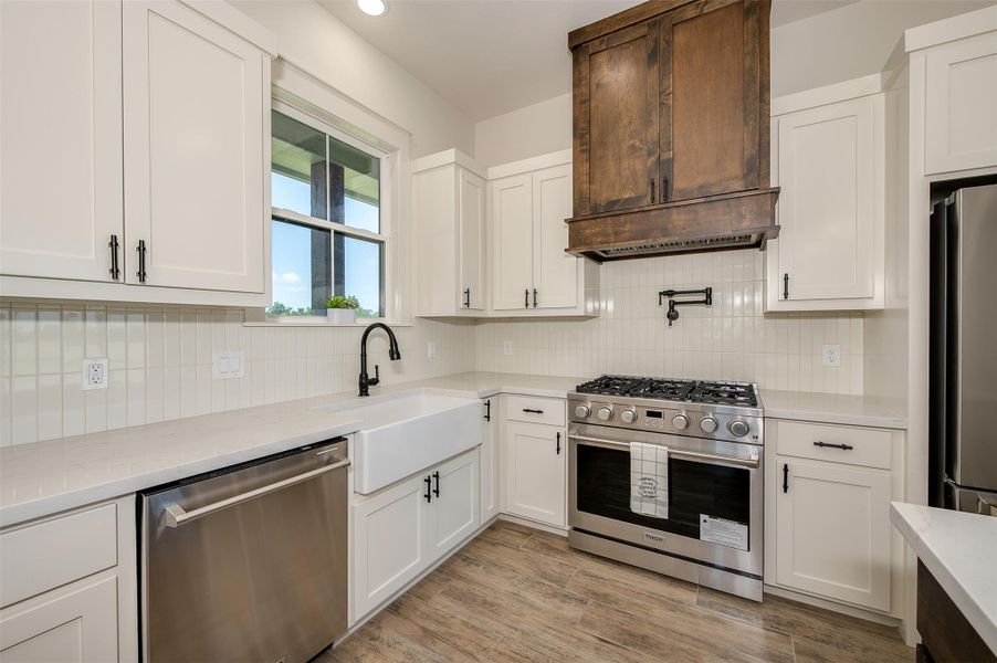 Kitchen featuring stainless steel appliances, white cabinets, light stone countertops, light wood-style floors, and backsplash