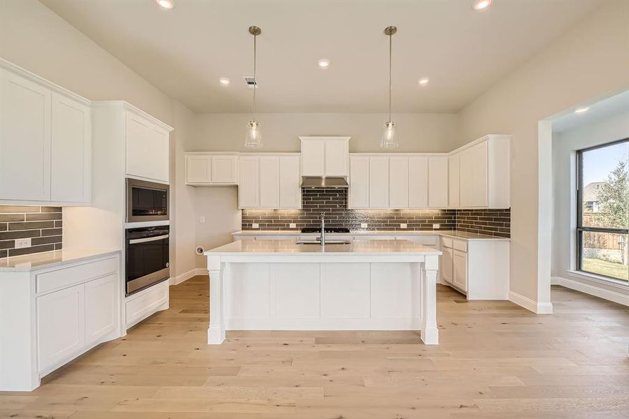 Kitchen with stainless steel oven, light hardwood / wood-style floors, a kitchen island with sink, and white cabinetry