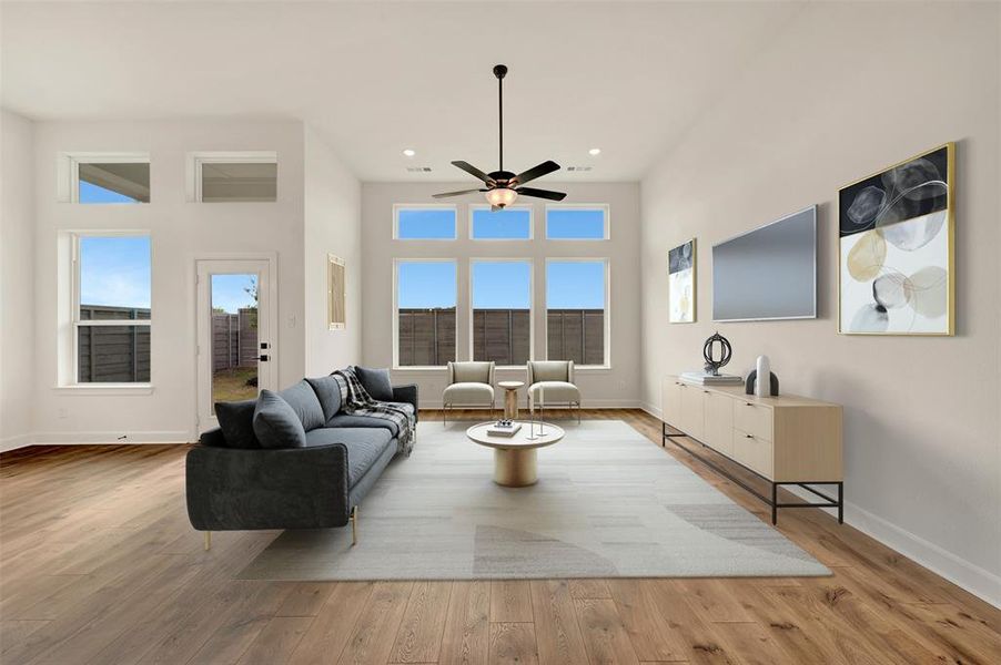 Spacious living area featuring high ceilings, wood-finish flooring, numerous windows, a contemporary ceiling fan, and direct access to the outdoor space