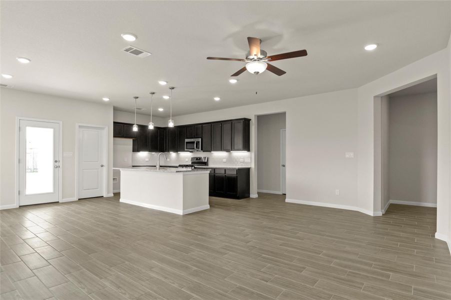Kitchen featuring appliances with stainless steel finishes, open floor plan, ceiling fan, light countertops, and an island with sink